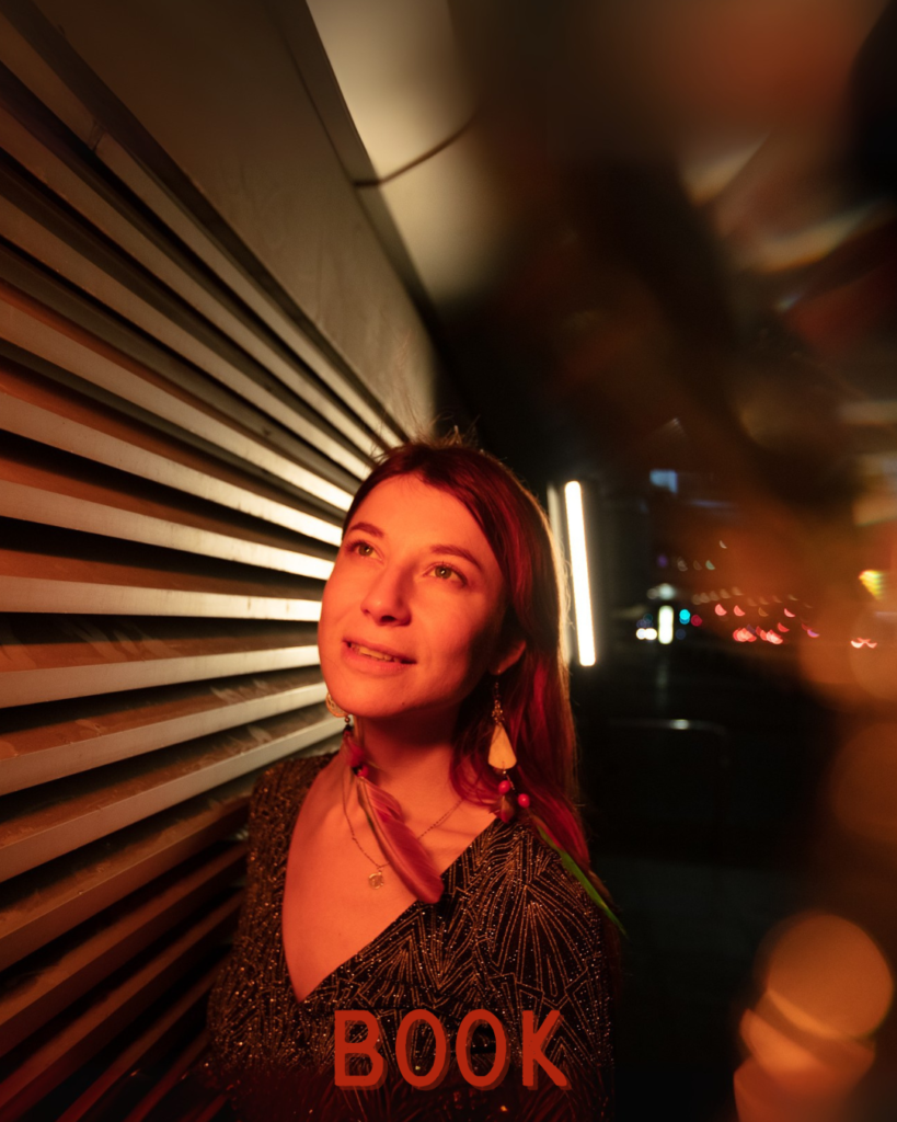 Seraphina Taylor smiling under warm golden light, standing near a metal wall with a thoughtful and inspired gaze.