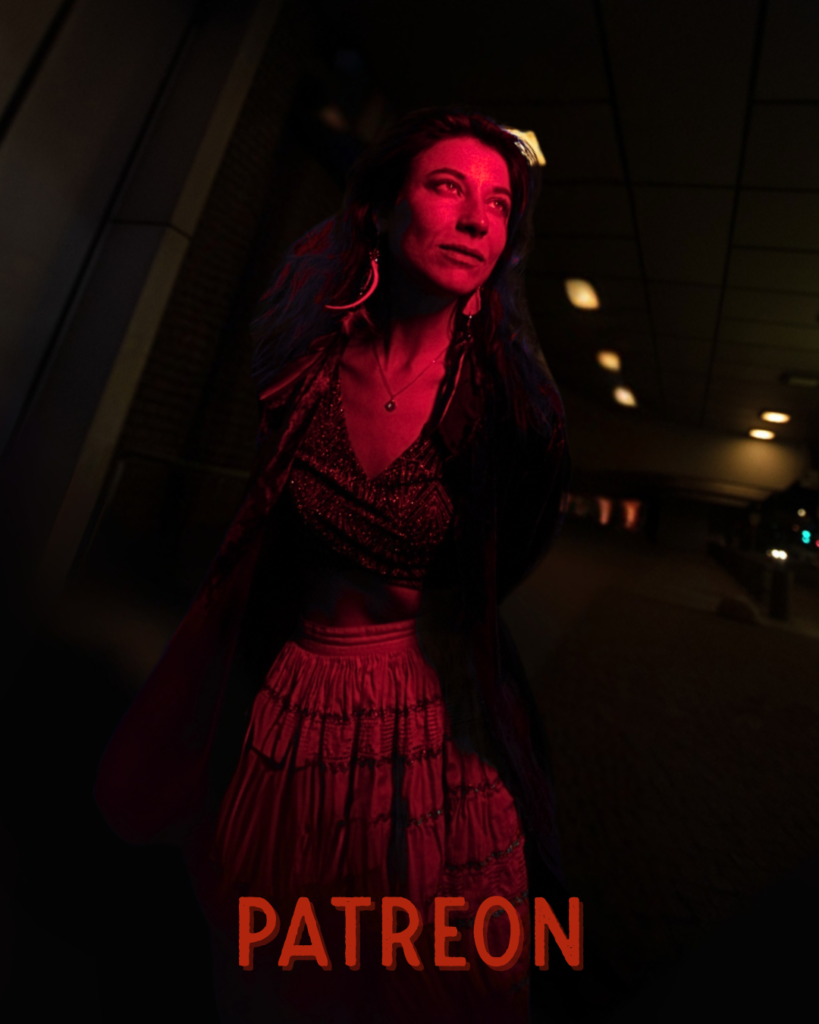 Seraphina Taylor standing in dramatic red light, wearing a flowing skirt and looking upward with creative intensity.